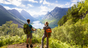 Two hikers at viewpoint in the mountains enjoying beautiful view of the valley with a lake and sunny warm weather in summer, green trees around